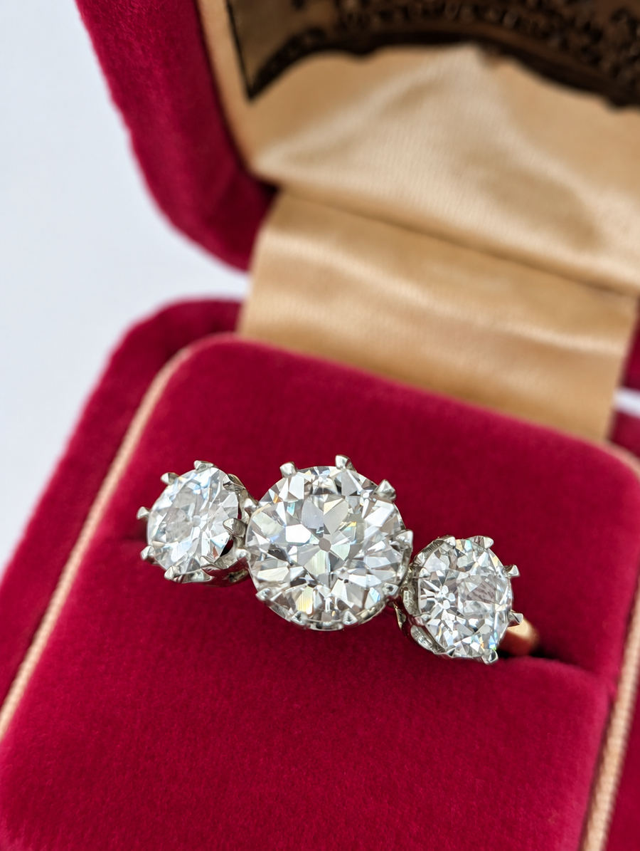 Close-up of a 3.05 carat old European cut three-stone diamond ring in a pink jewelry box against a white background
