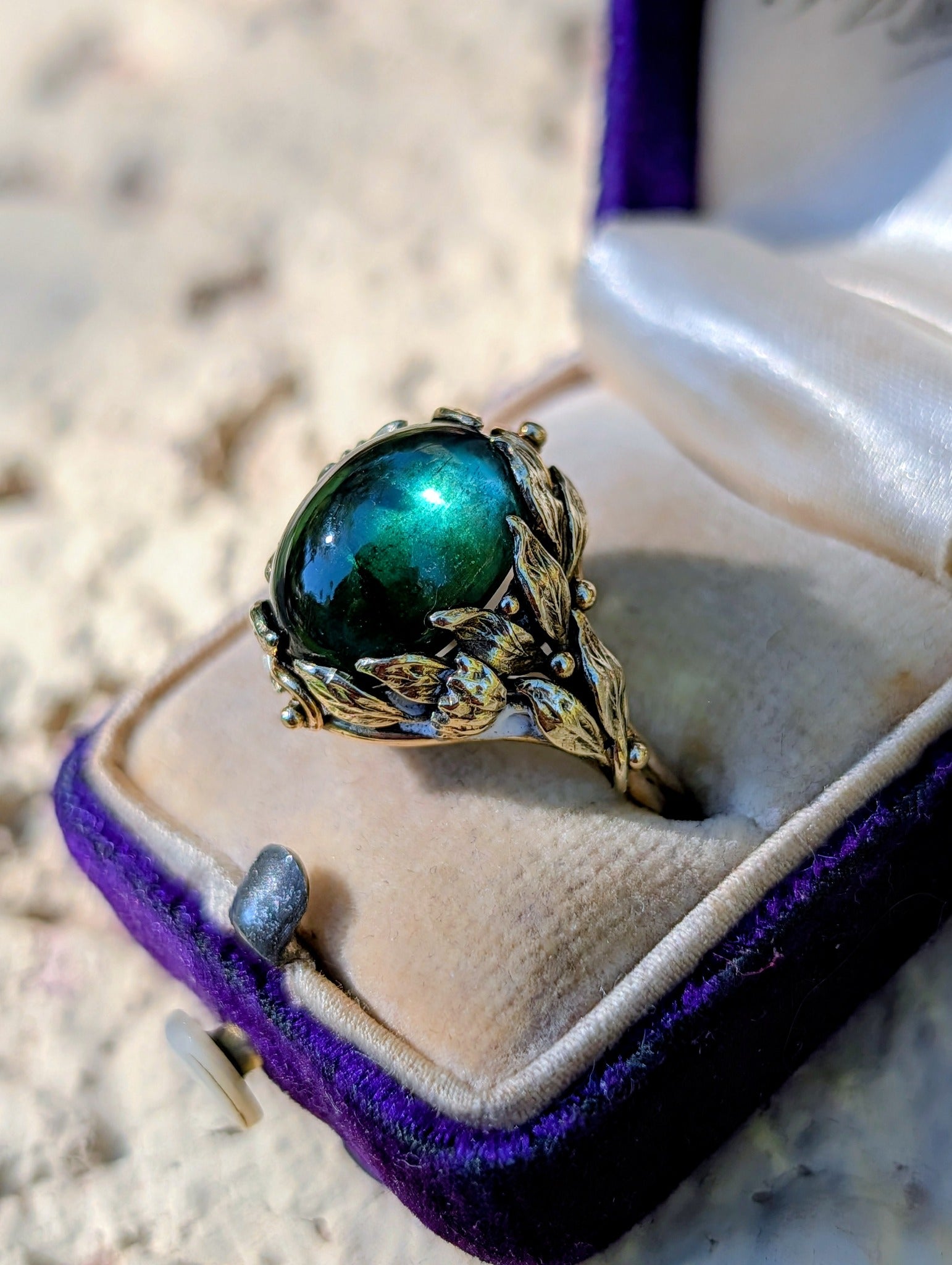 Angled view of green tourmaline cabochon and detailed gold leaves
