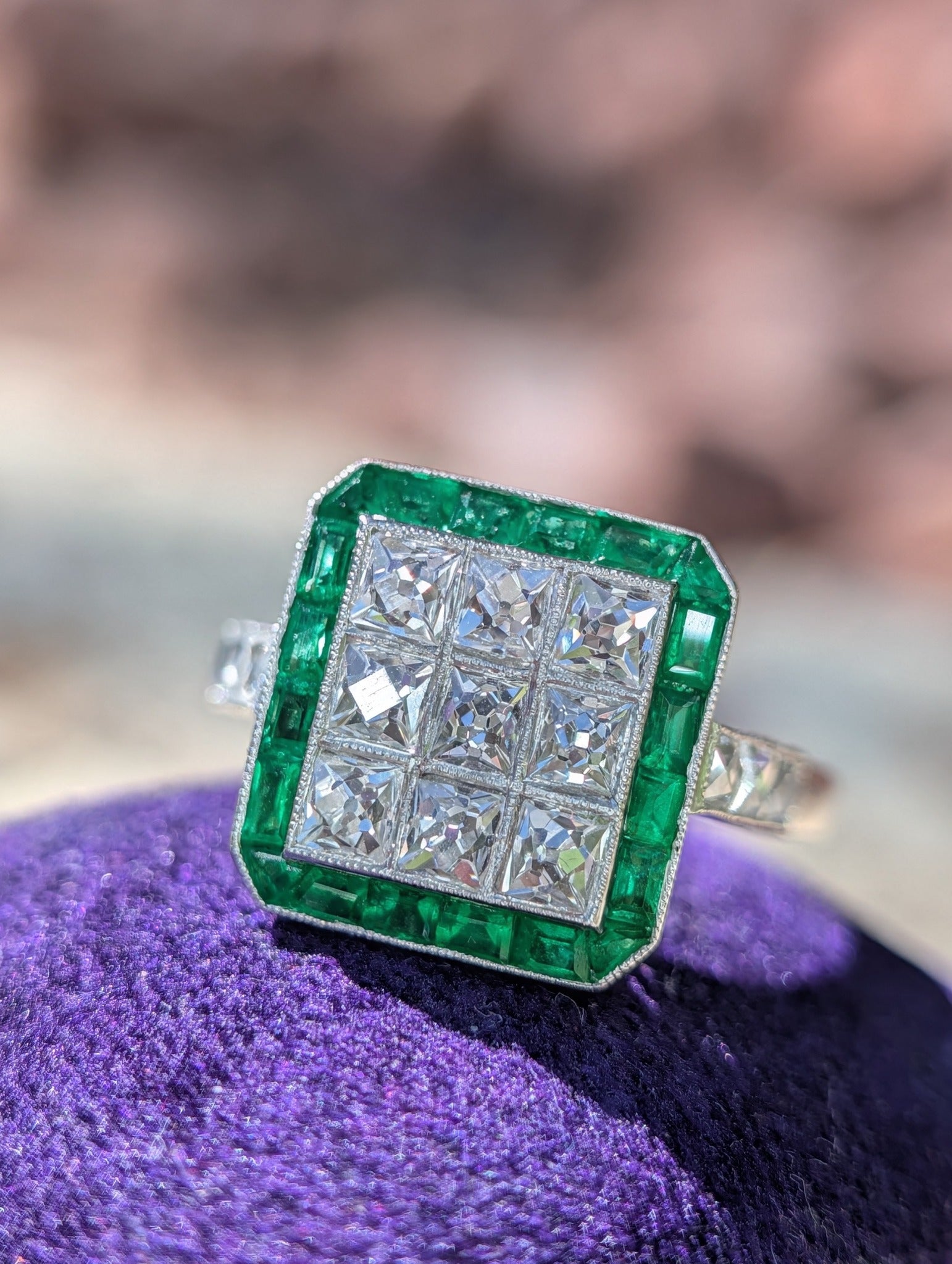 Front view of an Art Deco style platinum ring with French-cut diamonds and natural emeralds