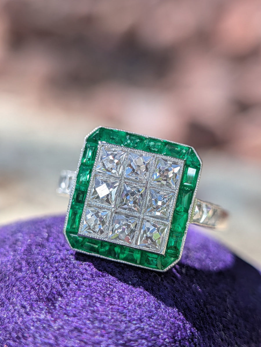 Front view of an Art Deco style platinum ring with French-cut diamonds and natural emeralds