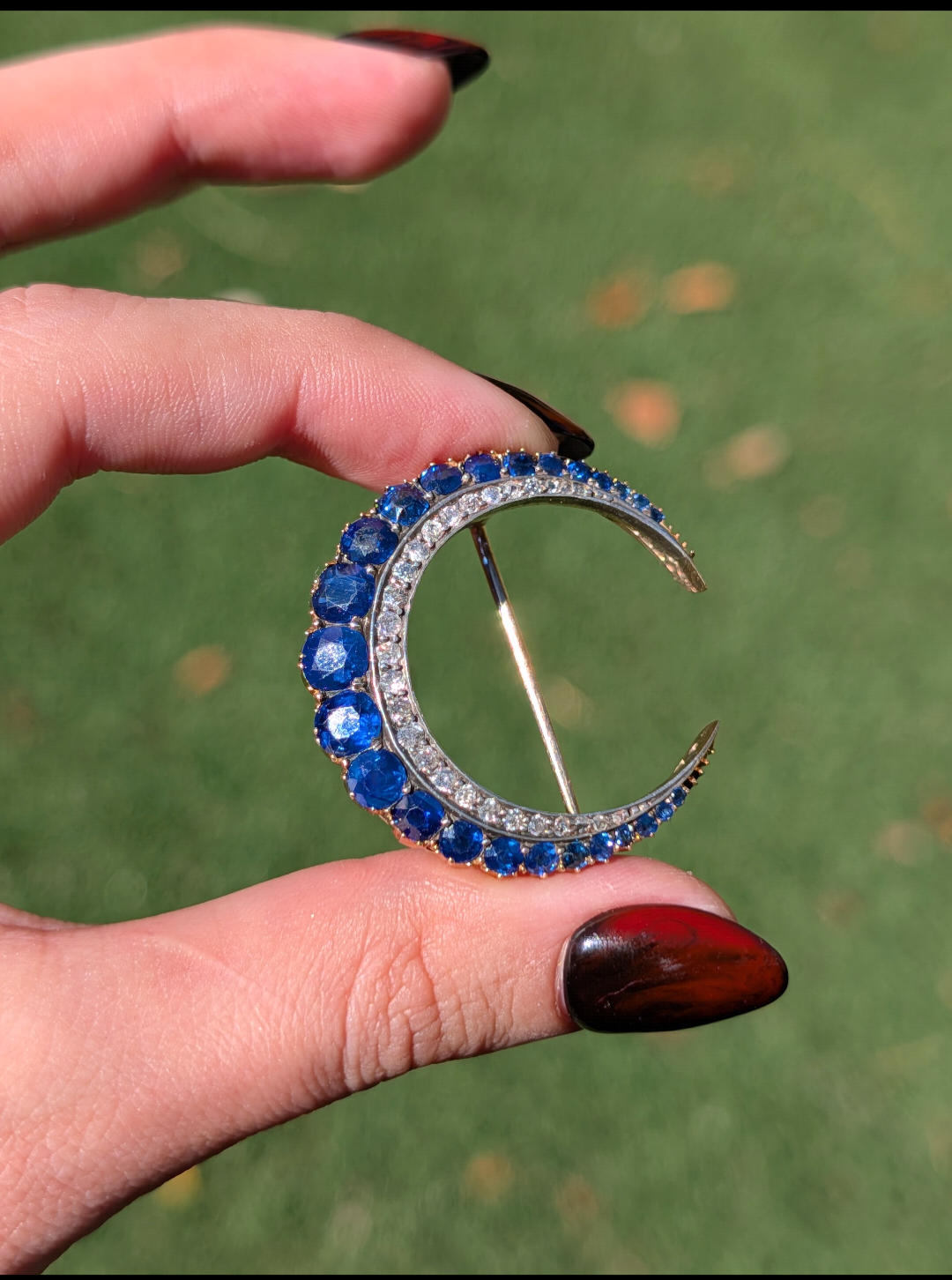 Antique Victorian sapphire crescent brooch held outdoors in natural sunlight